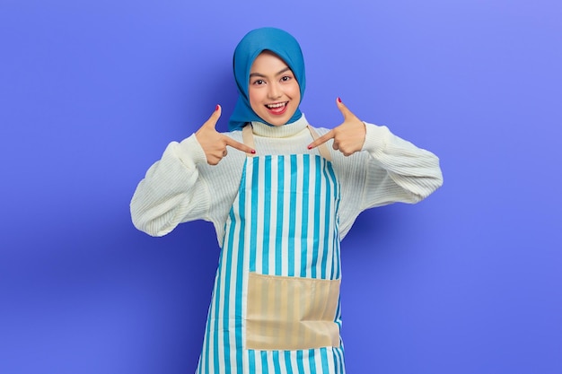 Ritratto di giovane donna musulmana asiatica sorridente in hijab e grembiule a righe che dorme con le mani piegate sotto le guance e gli occhi chiusi isolati su sfondo viola