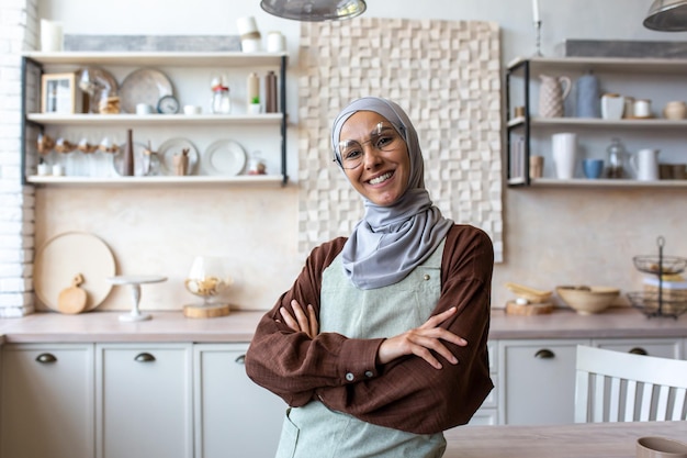 Ritratto di giovane donna musulmana food blogger coach chef in hijab in piedi a casa in cucina in grembiule