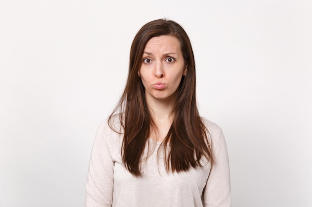 Ritratto di giovane donna offesa dispiaciuta sconcertata in abiti leggeri che soffia labbra isolate su sfondo bianco muro in studio. Persone sincere emozioni, concetto di stile di vita. Mock up spazio di copia.