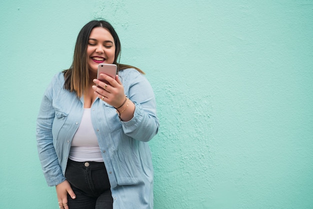 Ritratto di giovane donna plus size sorridente durante la digitazione di un messaggio di testo sul suo telefono cellulare all'aperto. Concetto di tecnologia.