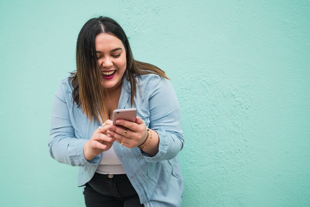 Ritratto di giovane donna plus size sorridente durante la digitazione di un messaggio di testo sul suo telefono cellulare all'aperto