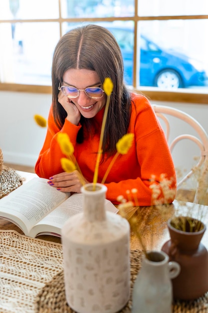 Ritratto di giovane donna positiva in abbigliamento casual che sorride e che legge un libro