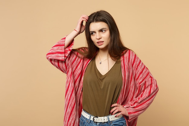 Ritratto di giovane donna preoccupata in abiti casual che guarda da parte, mettendo la mano sulla testa isolata su sfondo beige pastello in studio. Persone sincere emozioni, concetto di stile di vita. Mock up copia spazio.