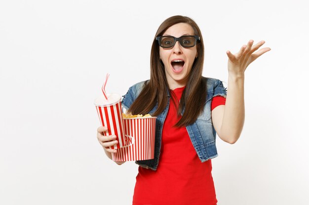 Ritratto di giovane donna scioccata in occhiali 3d che guarda film, tenendo secchio di popcorn e tazza di plastica di soda o cola, allargando la mano isolata su sfondo bianco. Emozioni nel concetto di cinema.