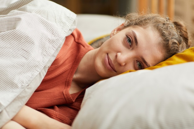 Ritratto di giovane donna sdraiata sul cuscino guardando davanti mentre riposa nel suo letto a casa