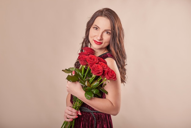 Ritratto di giovane donna soddisfatta in abito rosso con bouquet di rose