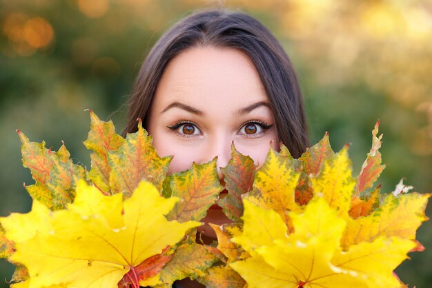 Ritratto di giovane donna sorridente con foglie d'autunno davanti al fogliame