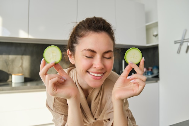 Ritratto di giovane donna sorridente felice in cucina che cucina tagliando le zucchine che tengono le verdure