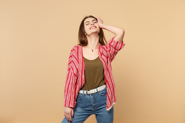 Ritratto di giovane donna sorridente in abiti casual che guarda la macchina fotografica che mette mano sulla testa isolata sul fondo della parete beige pastello in studio. Concetto di stile di vita di persone sincere emozioni. Mock up copia spazio.