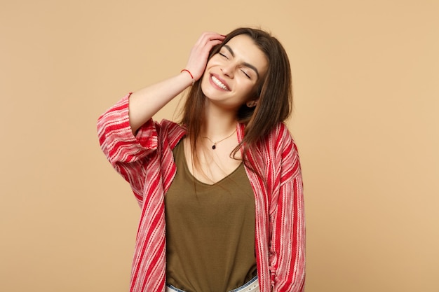 Ritratto di giovane donna sorridente in abiti casual che tiene gli occhi chiusi mettendo la mano sul viso isolato su sfondo beige pastello in studio. Concetto di stile di vita di persone sincere emozioni. Mock up copia spazio.