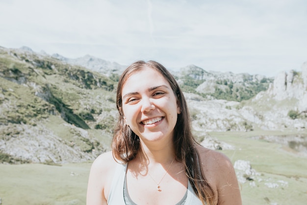 Ritratto di giovane donna sorridente viso parzialmente coperto di capelli volanti in una giornata ventosa in piedi in montagna - donna spensierata