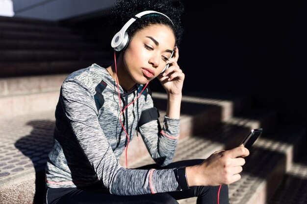 Ritratto di giovane donna sportiva e in forma che ascolta musica con il telefono cellulare.