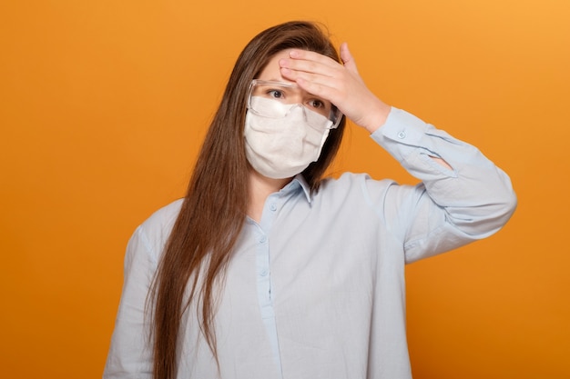 Ritratto di giovane donna sulla parete arancione in maschera protettiva medica con febbre