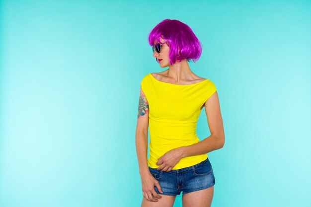 Ritratto di giovane donna transgender con pelle problematica in parrucca rosa e occhiali da sole a forma di cuore su sfondo blu