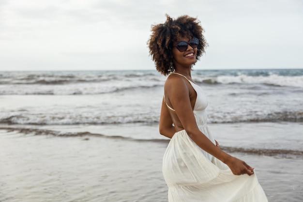 Ritratto di giovane e bella donna africana sorridente felicemente con abito bianco e sfondo spiaggia