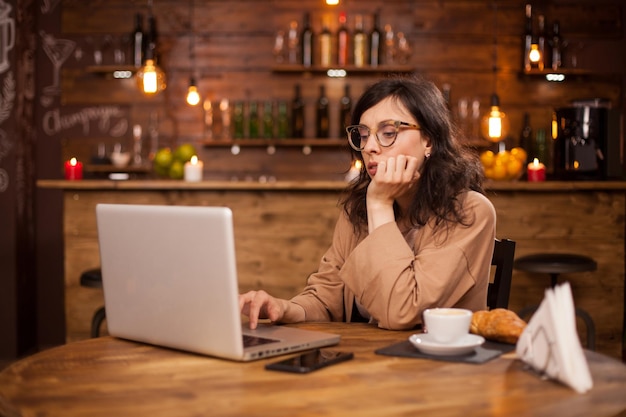 Ritratto di giovane e bella donna che lavora al suo computer portatile in una caffetteria. Ritratto di donna intelligente che lavora al computer portatile. Donna che lavora al suo computer portatile in una caffetteria con wifi.