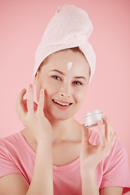 Ritratto di giovane e bella donna con un asciugamano sulla testa, applicare la crema idratante da giorno sul viso