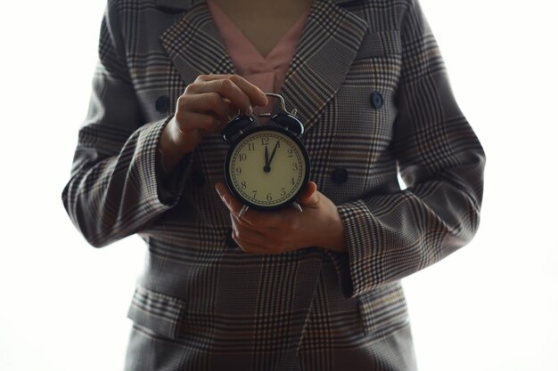 Ritratto di giovane e bella donna d'affari che tiene in mano orologio sfondo bianco disciplina e concetto puntuale