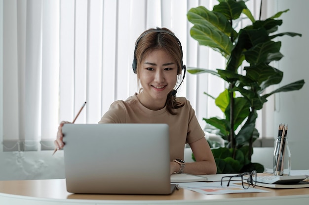 Ritratto di giovane e bella donna d'affari sorridente con le cuffie che lavorano nella moderna scrivania dell'ufficio utilizzando il computer Concetto di telemarketing e-commerce freelance di marketing online dipendente di uomini d'affari