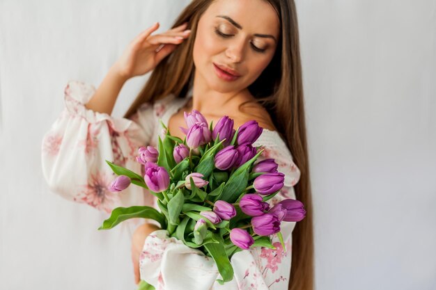 Ritratto di giovane e bella donna sexy con i capelli lunghi Modello con un bouquet di tulipani lilla su bianco Vacanze primaverili