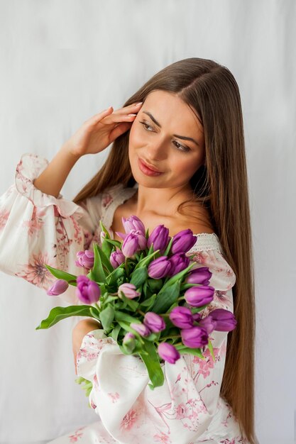 Ritratto di giovane e bella donna sexy con i capelli lunghi Modello con un bouquet di tulipani lilla su bianco Vacanze primaverili