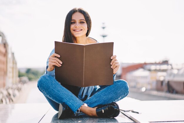 Ritratto di giovane e bella ragazza hipster in possesso di un libro di testo con copia spazio per la pubblicità