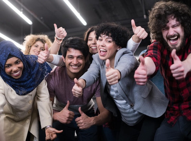 ritratto di giovane eccitato team aziendale multietnico di sviluppatori di software in piedi e guardando la telecamera mentre celebra il successo nel moderno ufficio di avvio