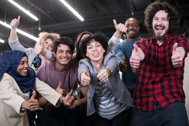 ritratto di giovane eccitato team aziendale multietnico di sviluppatori di software in piedi e guardando la telecamera mentre celebra il successo nel moderno ufficio di avvio