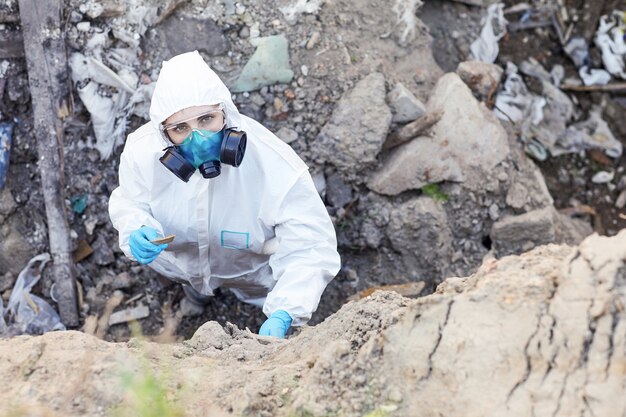 Ritratto di giovane ecologo in tuta protettiva che guarda l'obbiettivo mentre esamina le rocce