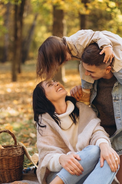 Ritratto di giovane famiglia felice che si siede insieme sul plaid nel parco di autunno