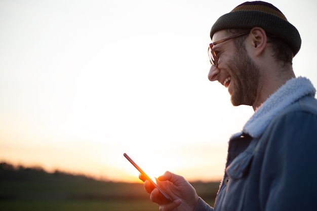 Ritratto di giovane felice con lo smartphone in mano sullo sfondo del tramonto