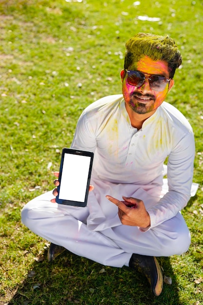 Ritratto di giovane felice indiano sul festival di colori holi utilizzando il telefono cellulare