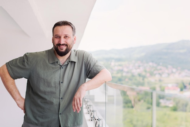 Ritratto di giovane hipster felice di successo in piedi su un balcone moderno con vista sulla città sullo sfondo