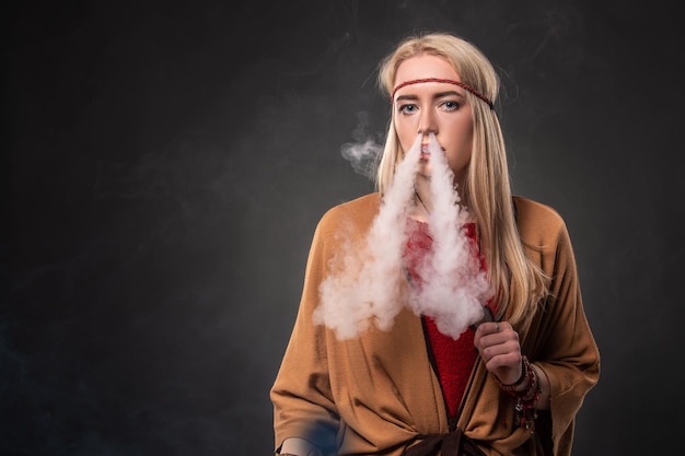 Ritratto di giovane hipster sexy che fuma ragazza vaping. La donna è vestita nello stile di un boho. Concetto di vapore. Svapare la sigaretta elettronica.