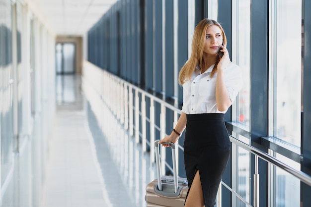 Ritratto di giovane imprenditrice attraente parlando sullo smartphone con la sua valigia in aeroporto