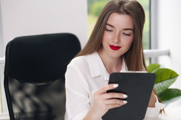 Ritratto di giovane imprenditrice indossando la camicia bianca seduto in un ufficio moderno con il computer portatile