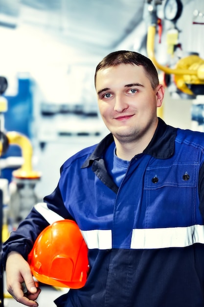 Ritratto di giovane ingegnere con casco nell'ambiente di lavoro in fabbrica Il lavoratore di gas guarda con sicurezza direttamente nella fotocamera