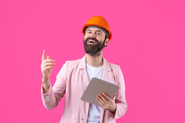 Ritratto di giovane ingegnere edile indossare elmetto arancione in una giacca rosa in piedi su sfondo rosso studio Un uomo con un tablet nelle sue mani