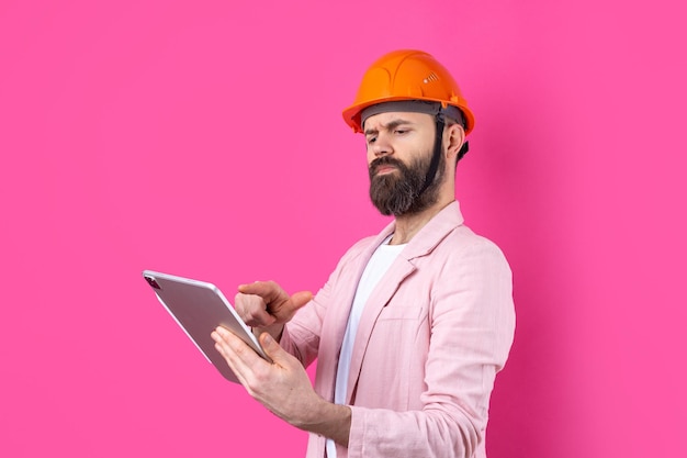 Ritratto di giovane ingegnere edile indossare elmetto arancione in una giacca rosa in piedi su sfondo rosso studio Un uomo con un tablet nelle sue mani