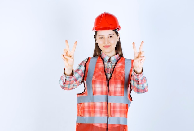 Ritratto di giovane ingegnere femminile in casco che dà segno di vittoria.
