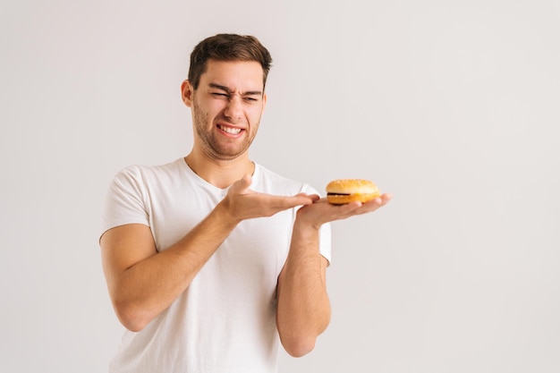 Ritratto di giovane insoddisfatto con disgusto che indica un hamburger cattivo su sfondo bianco isolato