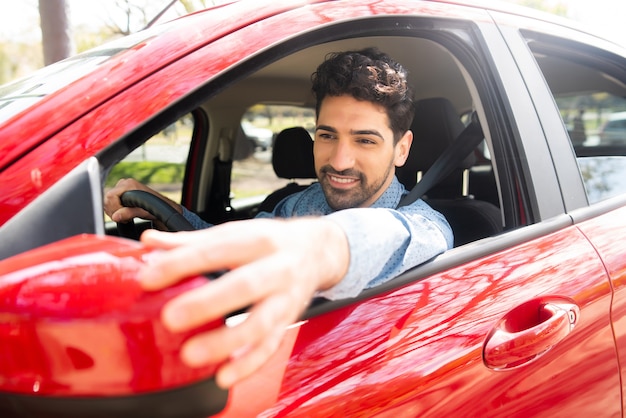Ritratto di giovane maschio alla guida della sua auto e specchietto retrovisore in movimento.