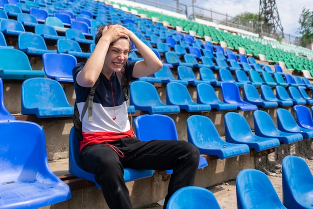 Ritratto di giovane maschio emotivo seduto sullo stadio sportivo durante gli eventi della partita