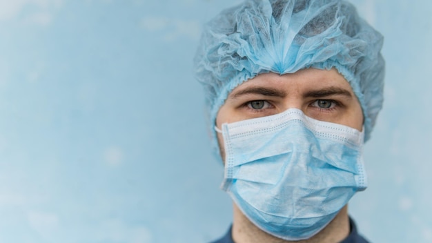 Ritratto di giovane medico con maschera medica blu e cappuccio Primo piano