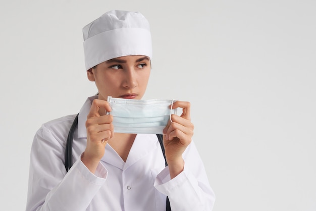 Ritratto di giovane medico femminile che indossa la maschera di protezione medica protettiva sulla parete bianca, spazio della copia