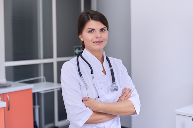 Ritratto di giovane medico femminile sicuro con lo stetoscopio con le braccia attraversate