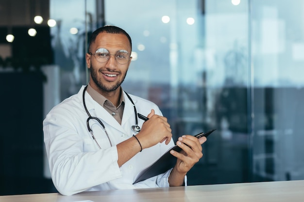 Ritratto di giovane medico latinoamericano bello che si siede nell'ufficio che tiene una penna con