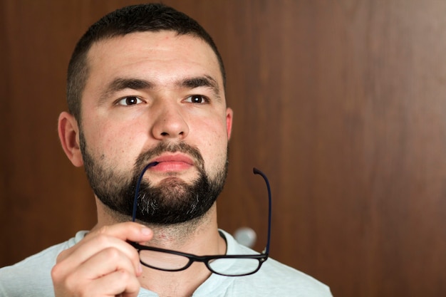 Ritratto di giovane moderno intelligente dai capelli neri barbuto bello in vetri con taglio di capelli corto e occhi neri gentili sorridenti su sfondo sfocato. Concetto di gioventù e fiducia.