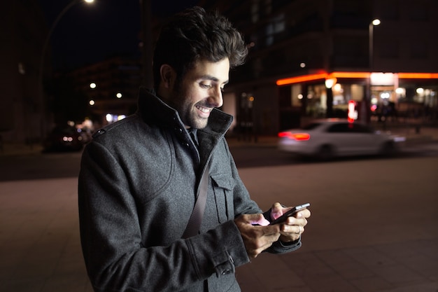 Ritratto di giovane moderno utilizzando il suo telefono cellulare in strada di notte.