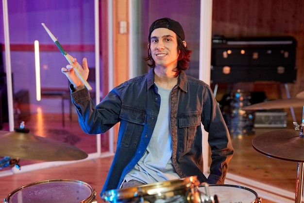 Ritratto di giovane musicista di talento che suona la batteria in studio di registrazione e sorridente